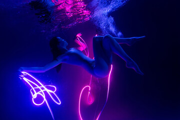 Sensual girl shows underwater performance in neon light. Soft blurred focus