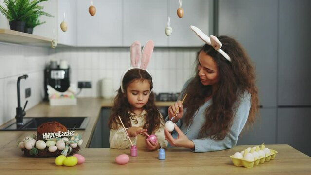 A mother and daughter in kitchen sitting, painting eggs for traditional spring dinner. A happy family is preparing for easter. Easter, family, holiday and children concept