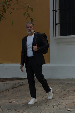 Attractive gray-haired man dressed in black suit walking downtown with black backpack