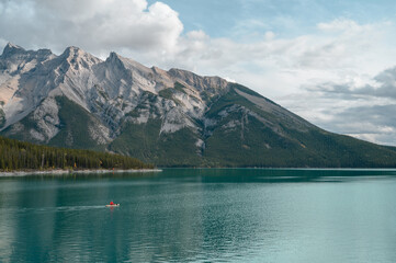 Panoramic image of a lake in Canada, in summer, with crystal blue water and snow on the mountains in the background. A canoe in the center.