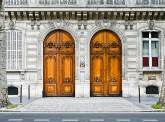 Paris ancient stone building entrance with carved doors, stone walls and balcony with trees in front