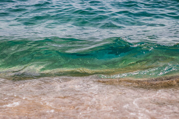 Beautiful close-up photo of clear blue and turquoise water wave with sand of the beach at the bottom