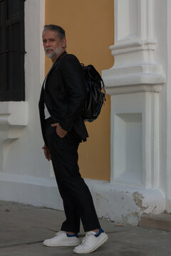 Attractive gray-haired man dressed in black suit walking downtown with black backpack