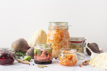 Fototapeta na wymiar Glass jars with various pickled vegetables and ingredients on a marble background