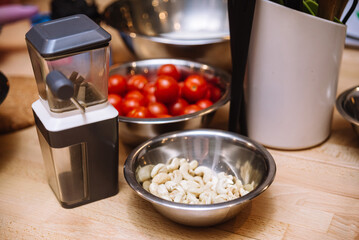 Ingredients of raw foods on the kitchen table before cooking. Raw cherry tomatoes, bowl of cashews, nut mill.
