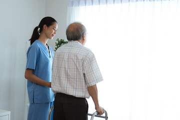 Happy smiling nurse in hospital and clinic uniform helping senior man with spectacles walk using a...