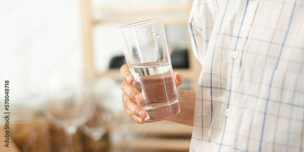 Wall mural Closeup of hands of senior male and female couple holding a glass of filled clear water on table while sitting and waiting at home