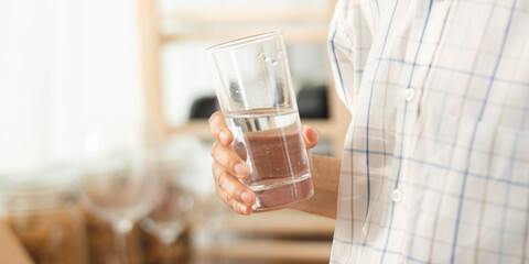 Closeup of hands of senior male and female couple holding a glass of filled clear water on table while sitting and waiting at home