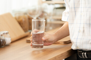 Closeup of hands of senior male and female couple holding a glass of filled clear water on table while sitting and waiting at home