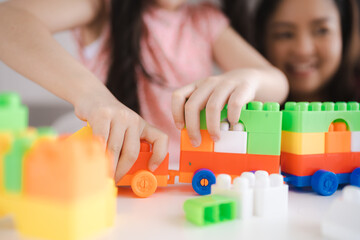 Cute little Asian daughter focused while playing and learning with smiling and cheerful mother with...