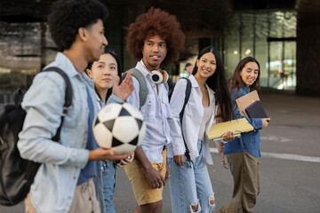 Fototapeta premium group of young diverse students with a ball walking through the city - focus on asian woman -