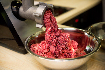 Minced meat comes out of the mincer in a metal bowl