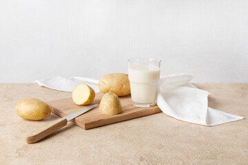 A glass of potato milk stands on a wooden board. There are unpeeled fresh potatoes nearby. Vegan product, vegetable milk. Copy space, horizontal orientation.