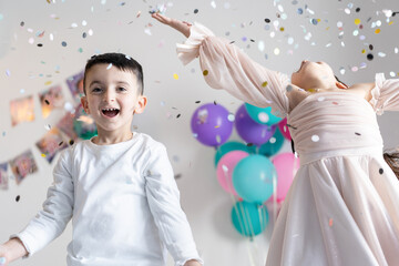 Two kids throwing colorful confetti and looking happy on birthday party.