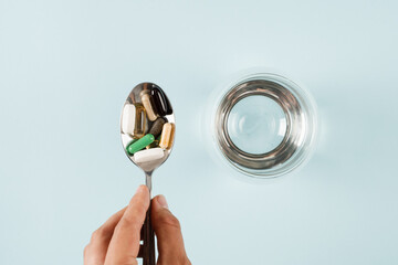 Pills on spoon of dietary biologically active supplements and glass of water for daily tablets...