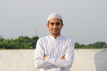 Young Asian Muslim boy looking at the camera wearing white shalwar kameez and cap. Muslim guy smiling wearing shalwar kameez.