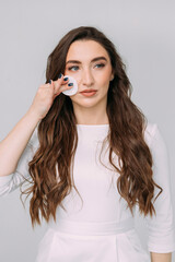 young long-haired girl washes off makeup with a cotton pad on a gray background