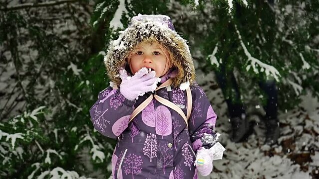 Little girl trying snow, slow motion. Happy child rejoices in winter on snow tree background. The child plays with snow in Prague park.