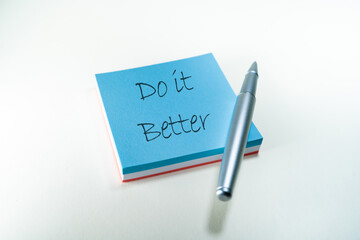 Do it better word writed in a blue post it with silver pen in the table. Improve and success concept.
