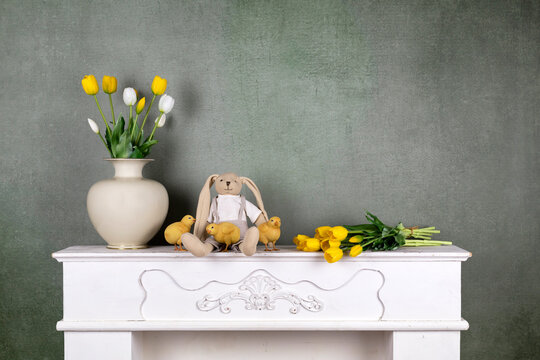 Easter still life with yellow and white tulips spring flowers, bunny toy and baby chickens on vintage green wall 