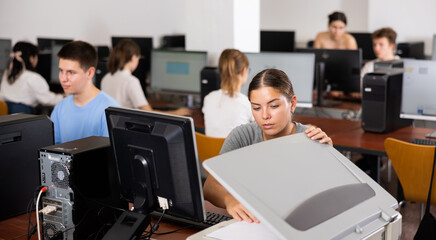 Interested girl student copying notes on copier while studying in college computer class