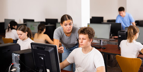 Fototapeta premium Concentrated female student explaining the topic to male friend while she is studying computer science on the pc in the classroom.
