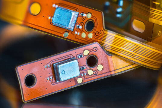 Beautiful flex electronic printed circuits on yellow and orange colored strips on black blurry background. Closeup of bendy PCB or small components on flexible ribbon cables from inside of headphones.