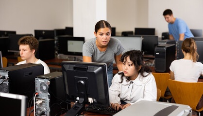 Schoolgirl using computer and teacher helping to him in classroom