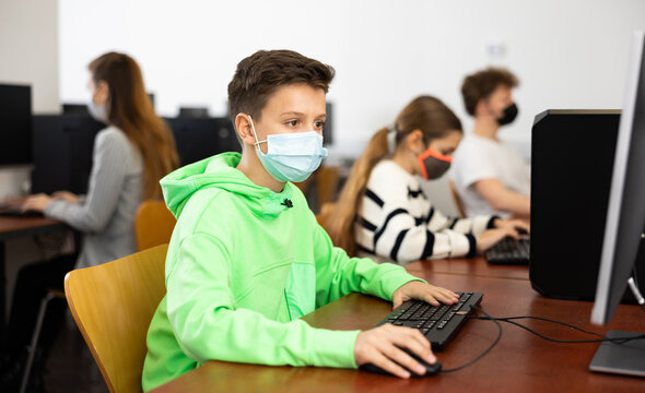 Positive Male Student Wearing Face Mask Working On Computer In Library. Concept Of Adult Self-education During Pandemic