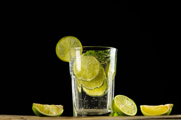Glass with water and limes on wooden table with copy space over black background
