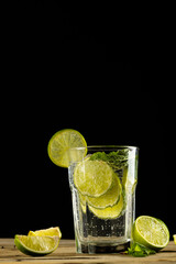 Glass with water and limes on wooden background with copy space over black background