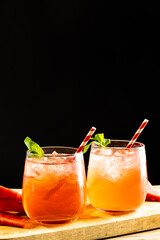 Glasses with cocktail and straws on wooden board with copy space over black background