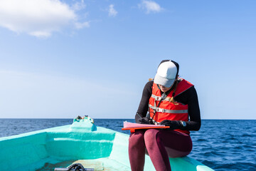 Marine biologist writing down data sitting on a boat - obrazy, fototapety, plakaty