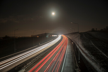 smugi świateł jadących nocą aut autostradą w świetle księżyca - obrazy, fototapety, plakaty