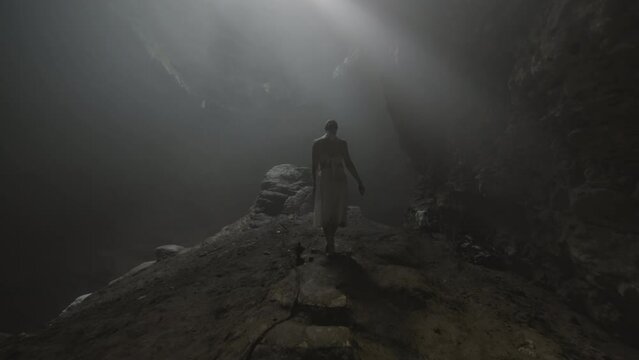 Woman Walking On Pathway In Deep Cave While Sunrays Passing Through Sinkhole - Java, Indonesia
