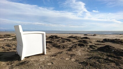 Luxury white lounge bar chair on empty sandy beach with washed out algae and view of sea and blue...