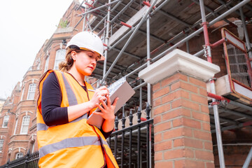 Chartered civil engineer woman writing on a tablet with electronic pen, hard hat and orange personal protective equipment, inspection, touchscreen, technology and innovation in construction site
