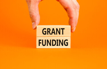 Grant funding symbol. Concept words Grant funding on wooden blocks. Beautiful orange table orange background. Businessman hand. Business and grant funding concept. Copy space.