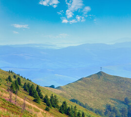 Summer misty mountain landscape with christian cross on top (Ukraine, Carpathian Mountains)