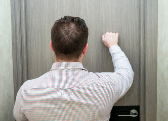 An elegant man, rear view from the back in a shirt is knocking on the office door to the director. A business man in a shirt knocks on the door.