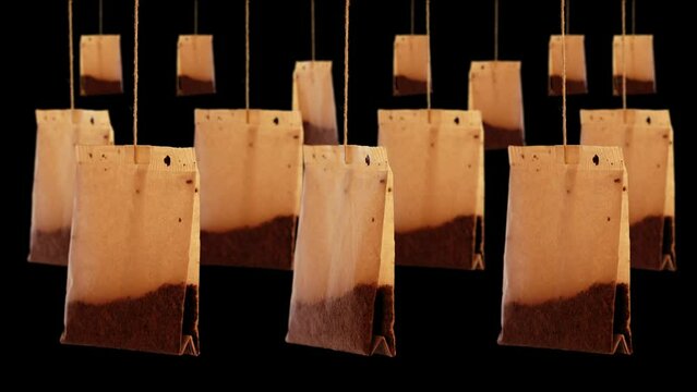 Numerous used brown paper teabags with natural herbal brew hang on thin threads swaying in wind on black background closeup