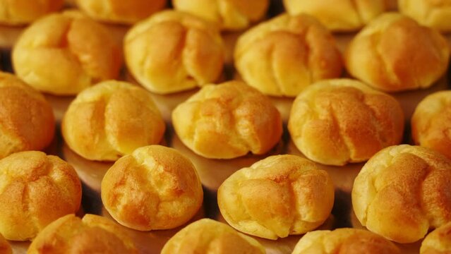 Motion over lines of delicious fresh beige eclair buns lying on shiny metal baking tray at bright light in kitchen closeup