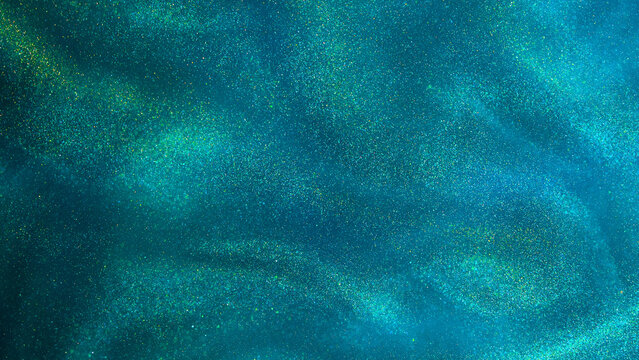 Various stains and overflows of gold particles in green fluid with blue tints. Golden particles dust and smooth defocused background. Liquid iridescent shiny backdrop with depth of field.