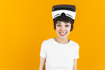 Positive VR experiences. Young female gamer looking at camera and smiling with virtual reality headset on her head. Orange background. High quality photo