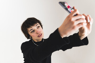 Soft grunge styled person taking selfie with smartphone in studio. Short-haired girl using her cellular. High angle view. High quality photo