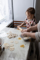 Little girl helping her grandmother with cooking russian dumplings at home