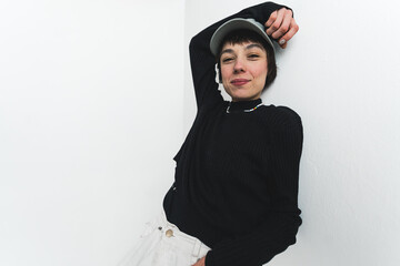 Female model leaning over white wall with one hand over her head. Modern autumn and winter fashion. Studio shot. High quality photo