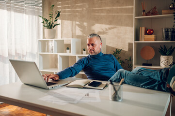 Middle aged man working in a home office and sitting with legs on a table