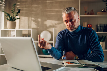 Middle aged man showing middle finger to a laptop screen while working at home