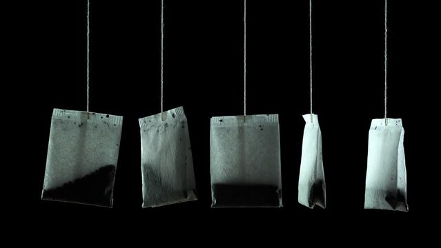 Set of new white dry paper tea bags with tasty Chinese brew hang turning on thin threads on black background close view